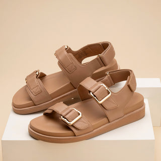 Pair of brown sandals with gold buckles on a beige background