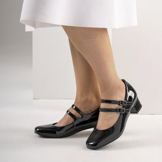 Black patent leather shoes worn with a white skirt on a light background