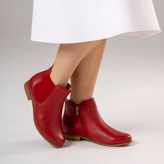 Red leather ankle boots worn with a white skirt on a light background